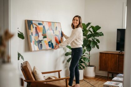 Femme souriante accrochant une toile dans un salon moderne